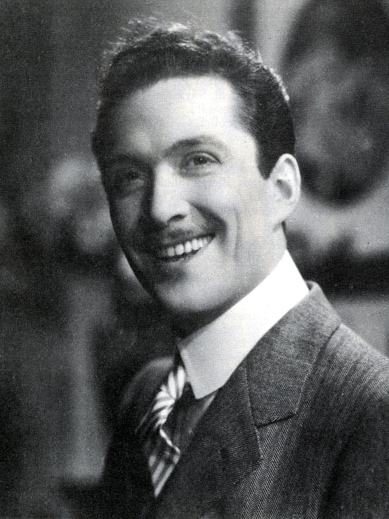 Black-and-white portrait shows Rodolfo Gucci as a young man, smiling towards the camera while wearing a sharp suit
