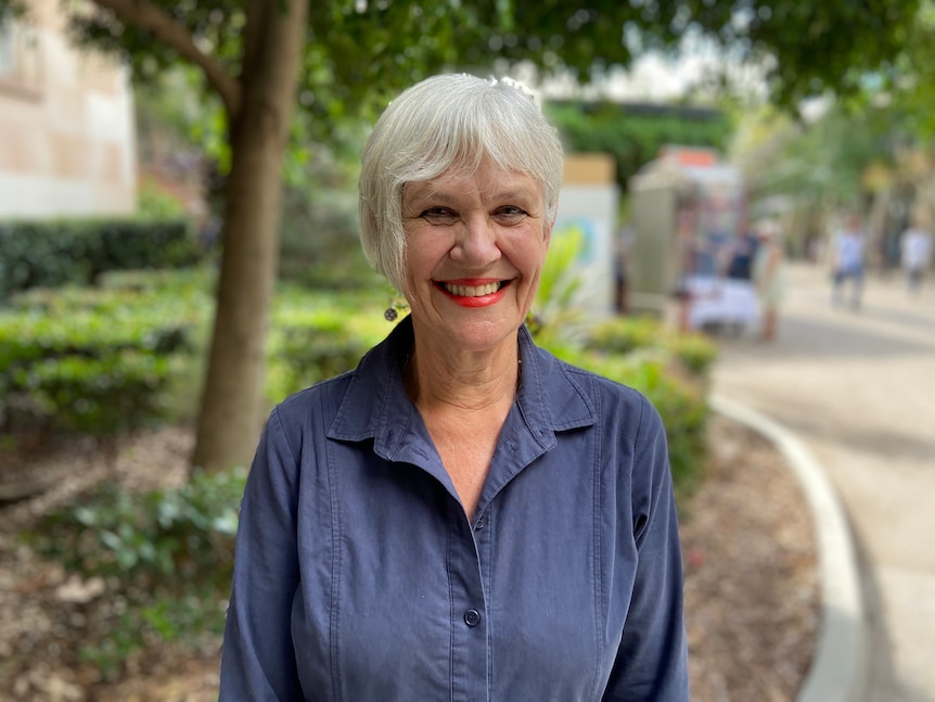 A woman with grey hair and bright smile looks into the camera.