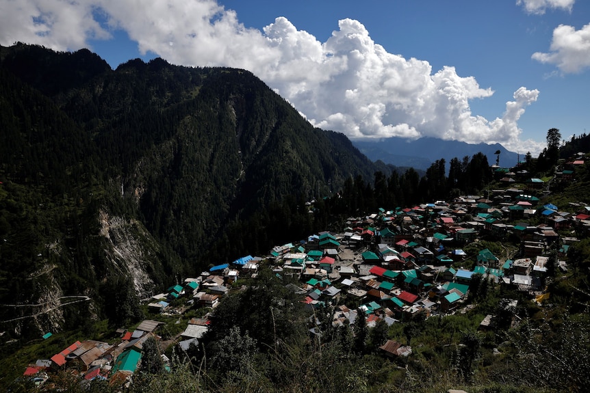 An aerial shot of a village with red and green roofs right near a mountain side.