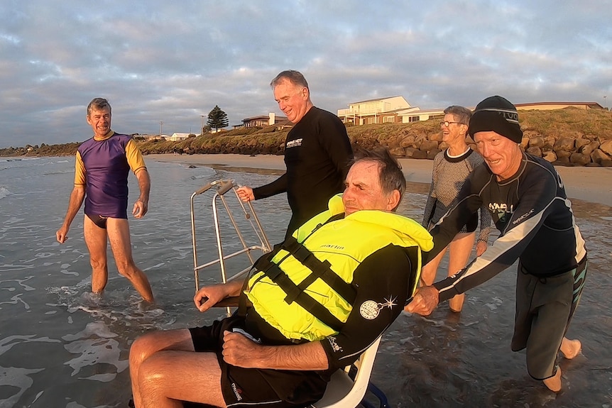 People in bathers laugh with Jim Pevitt as he is pushed into ocean