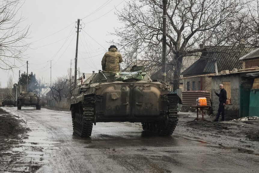 Ukrainian service members ride a tank on a deserted street.