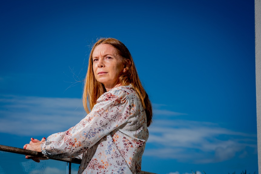 A woman looks out to distance while holding a balcony railing on a blue sky day