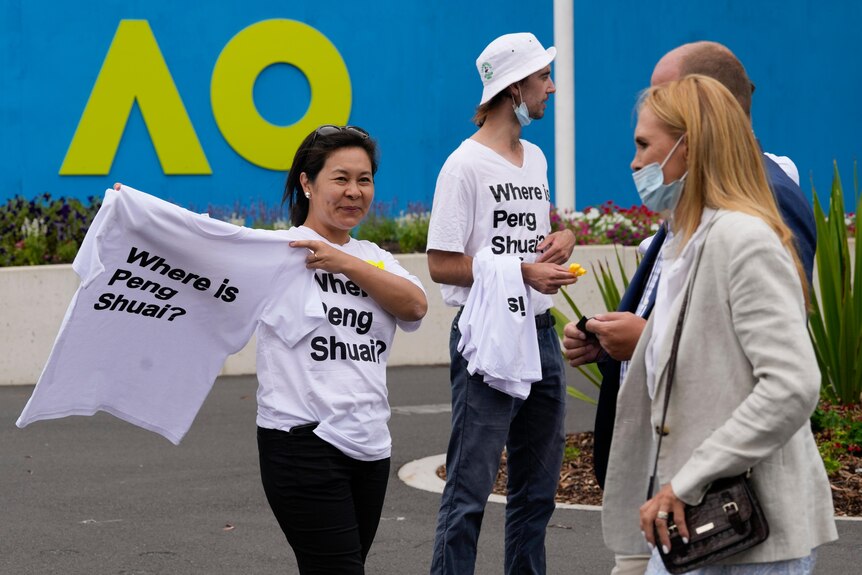 A woman handing  out a T shirt reading 'Where is Peng Shuai' with the Australian Open logo in the background.