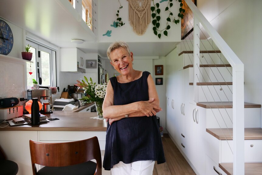 woman smiles at camera standing inkitchen with stairs leading up to her left