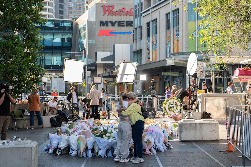 Two people embrace near floral tributes outside Westfield Bondi Junction