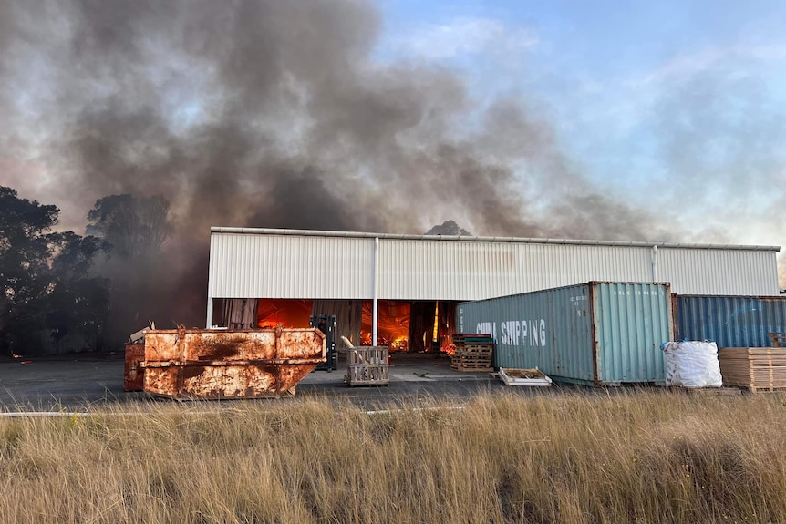 A fire burns in a large shed in a field.