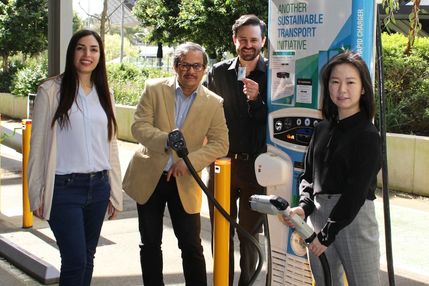 Two women and two men beside an EV charging station