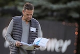 Lachlan Murdoch, wearing a black puffer jacket over a grey sweatshirt, looks at documents while walking