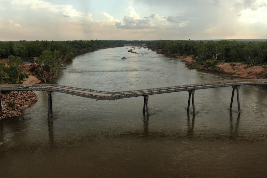 A badly damaged bridge sags over a river.