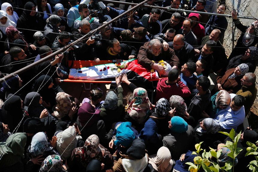 Crowds gather around the body of a man during a funeral procession.
