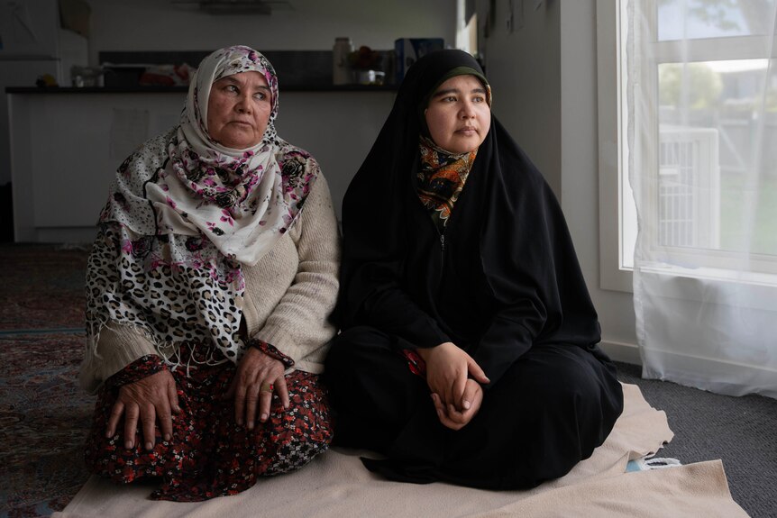 Two Hazara women seated in a room, while wearing traditional clothing.