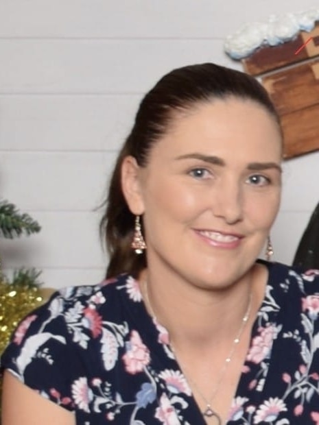 A woman smiling in front of a Christmas tree.