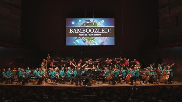 Orchestra on stage with illuminated sign that reads 'Bamboozled! Music by Paul Rissmann'