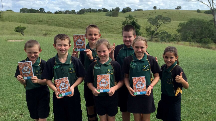 seven school children stand outside their school with copies of their DVD