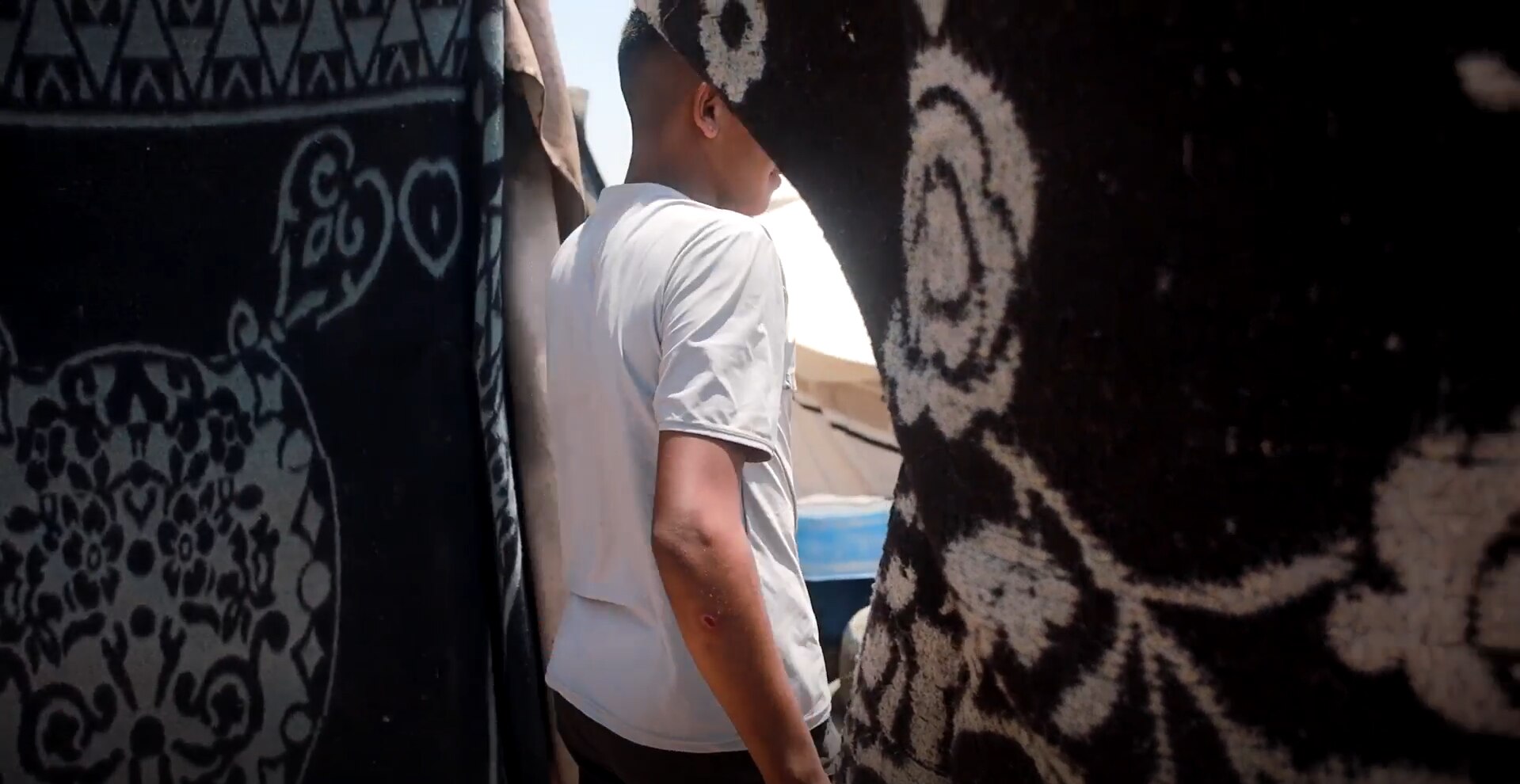 The back of a boy pushing a hanging rug aside as he walks