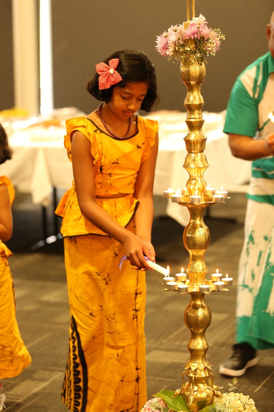 A girl in a yellow dress lights a candle as part of traditional celebrations