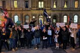 A group of people gather at night outside a building holding signs and the Eureka flag