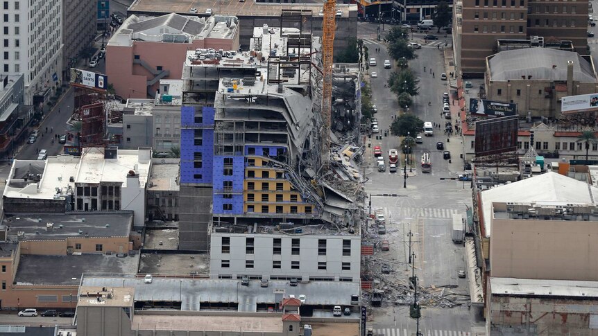 This aerial photo shows a building after a fatal partial collapse with a crane next to it there is also debris on the road below