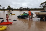 Man in h-vis unloads a jetski off a ute. A kid stands in front with a paddle and red kayak.
