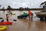 Man in h-vis unloads a jetski off a ute. A kid stands in front with a paddle and red kayak.