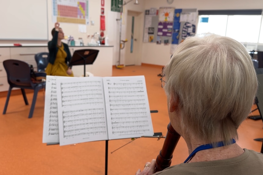 A grey haired woman plays along with the directions of her conductor at the recorder festival. 