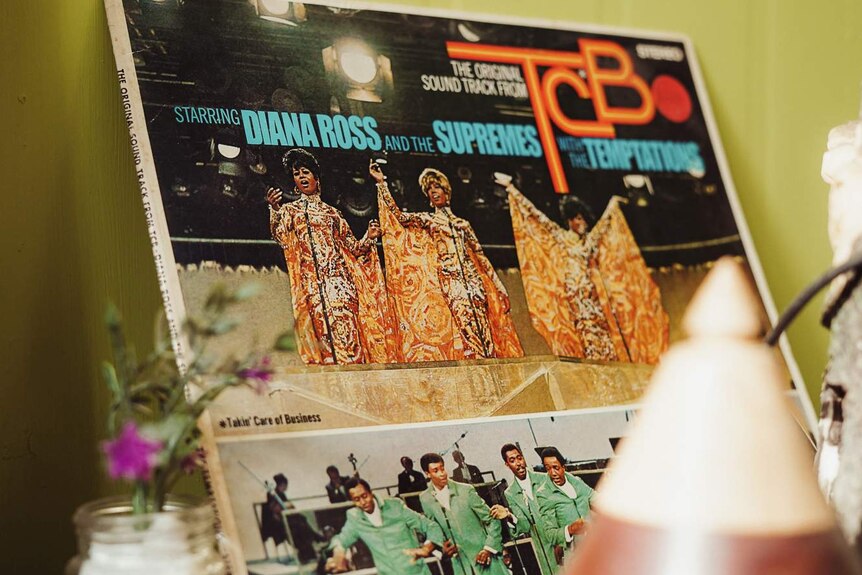 An old record sits on a shelf against a green wall. The record is the soundtrack from TCB starring Diana Ross and The Supremes.