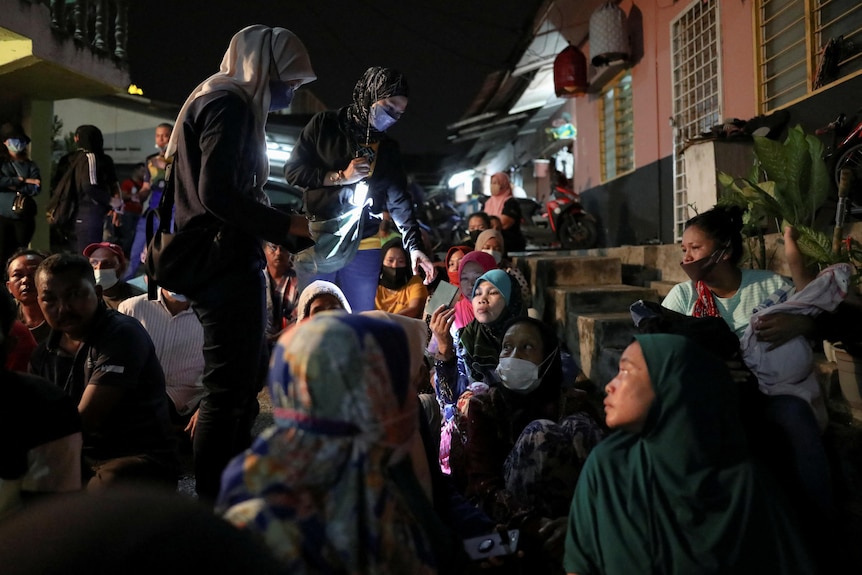 An immigration officer checks the documents of immigrants, who are sitting on the floor in Malaysia.