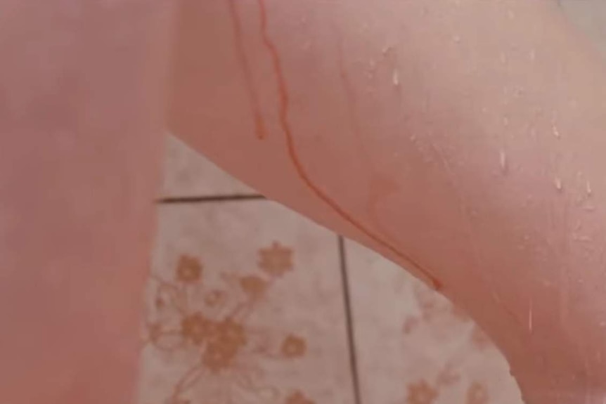 A close up shot shows blood and water running down the inside of a woman's leg while she is in the shower.