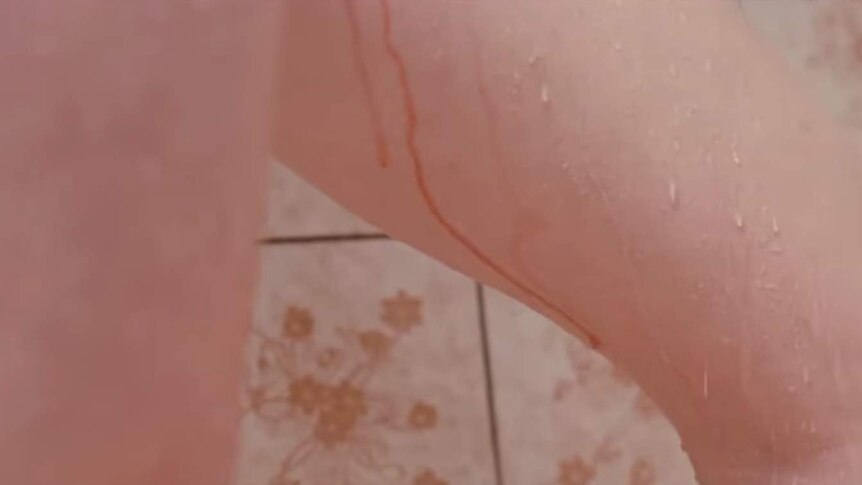 A close up shot shows blood and water running down the inside of a woman's leg while she is in the shower.