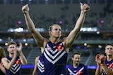 An AFL player lifts both arms into the air and gives a thumbs up to the crowd.