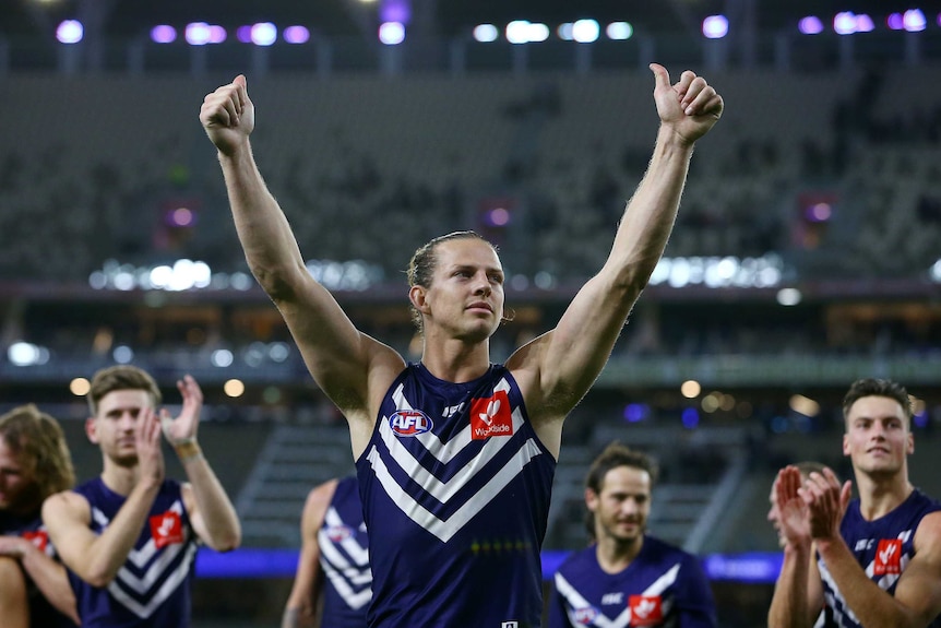 An AFL player lifts both arms into the air and gives a thumbs up to the crowd.