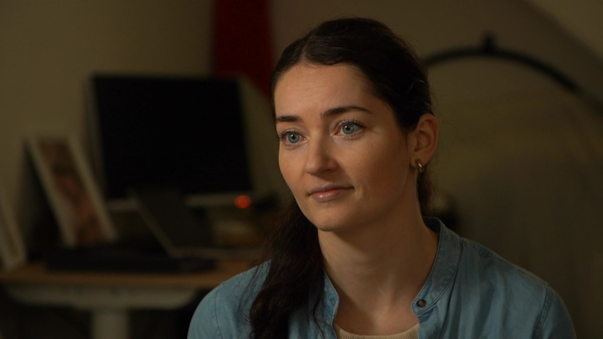 一位身穿蓝色衬衫、长着棕色长发的女士坐在家庭办公室里。