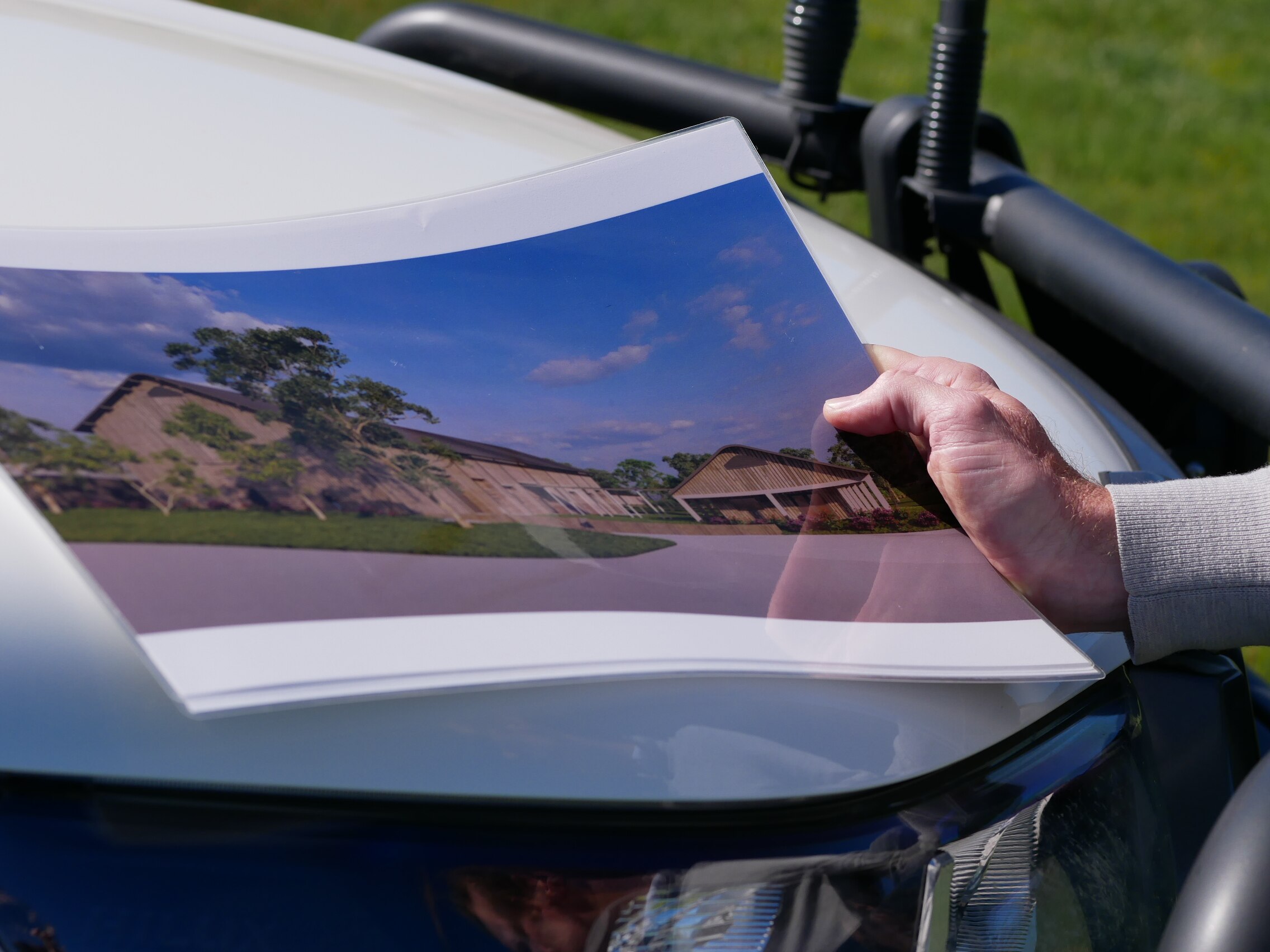 A hand holding a picture of an abattoir on the hood of a car. 