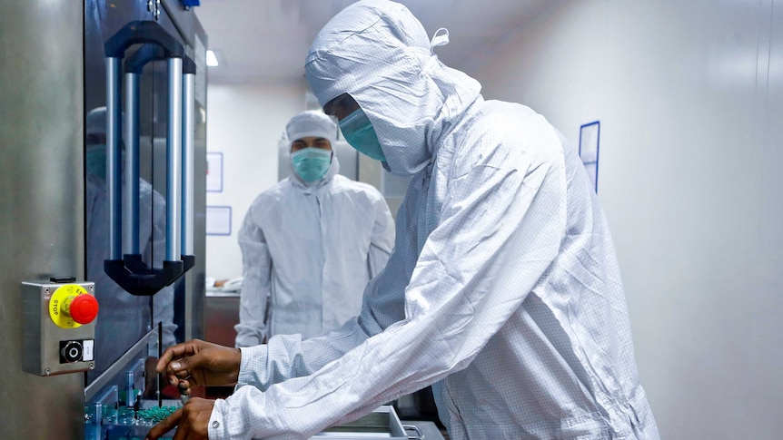 Two men in full PPE looking at a machine