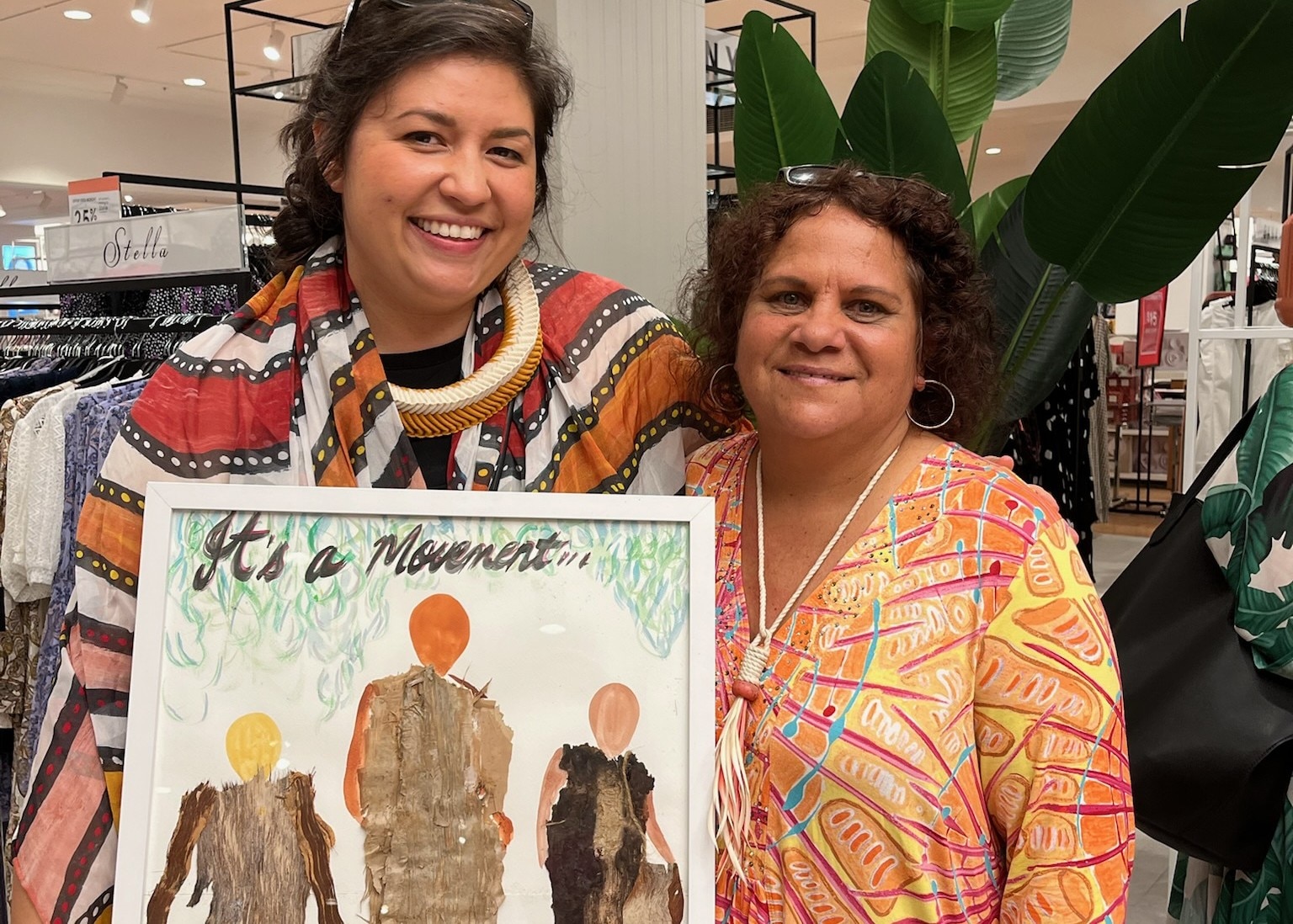 Duas mulheres lado a lado segurando uma foto emoldurada