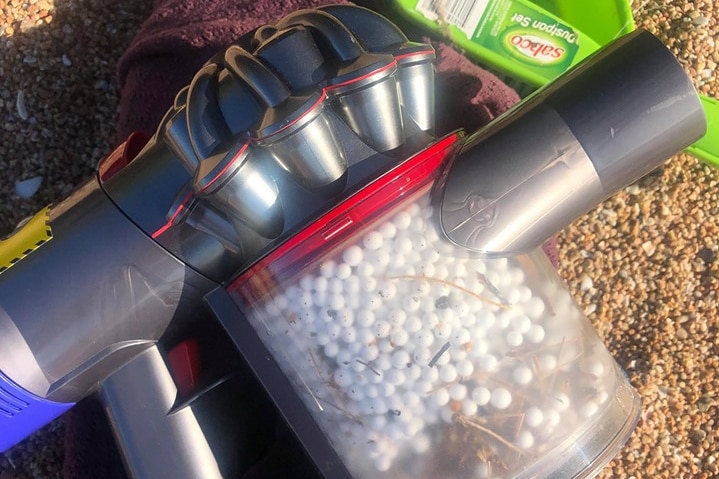 A vacuum cleaner rests on the beach, inside you can see hundreds of bean bag balls.