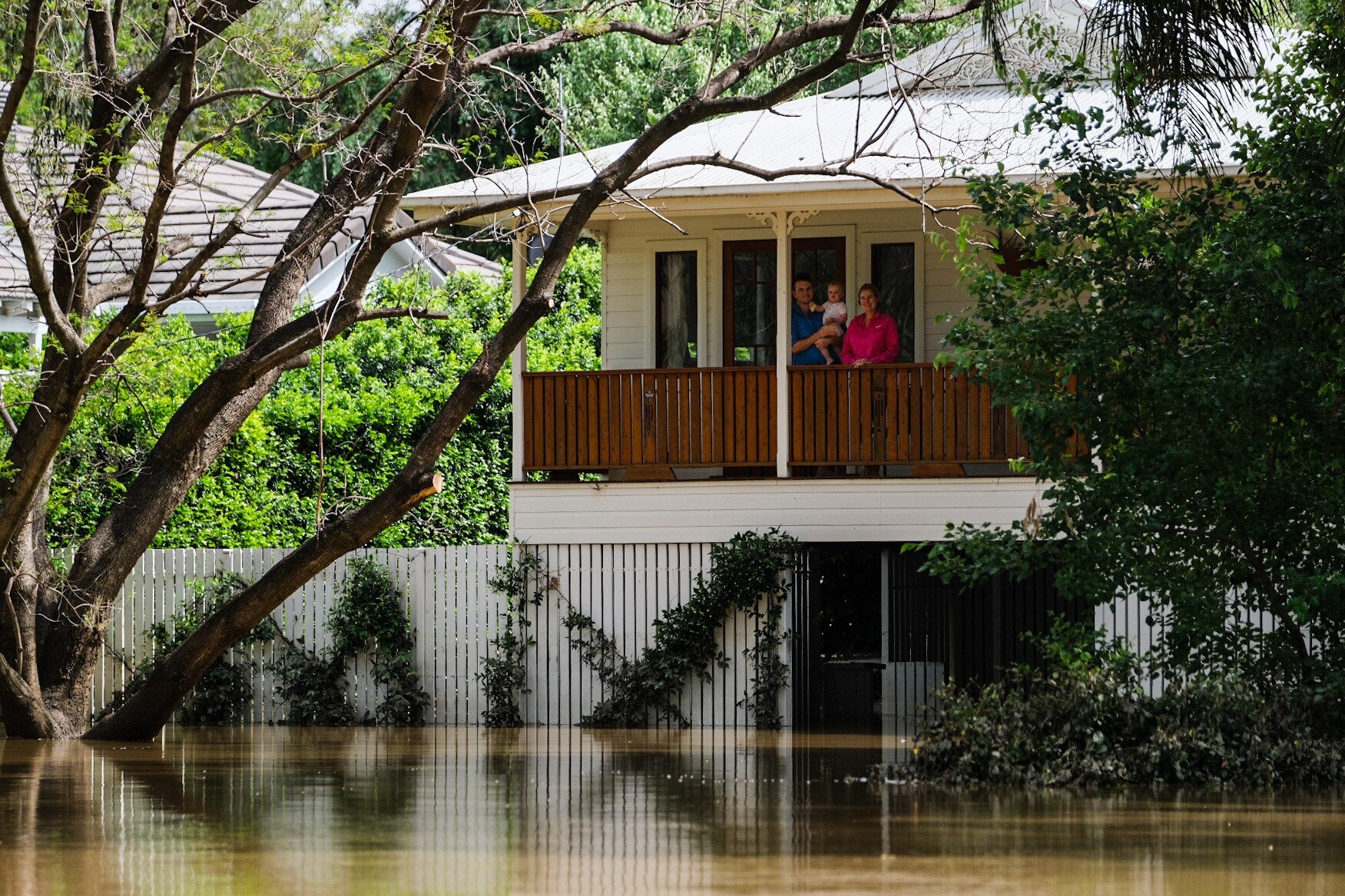 A family can be seen standing on their balcony from across a flooded street