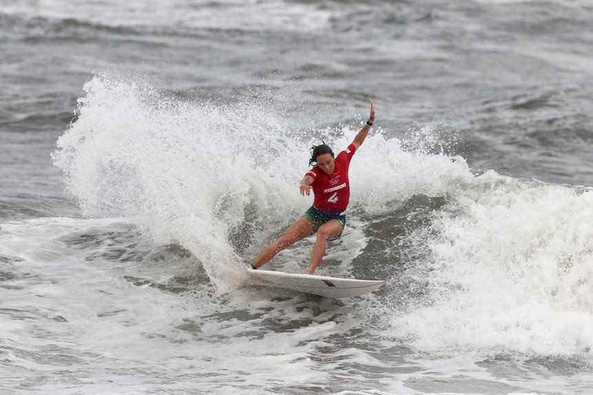 Una mujer vestida con un top rojo monta una tabla de surf en el océano