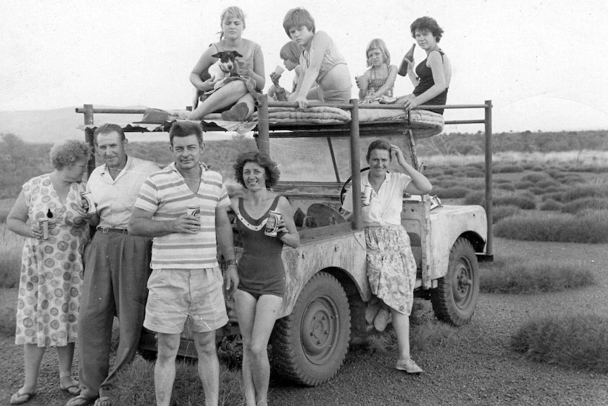 A black and white photo of people gathered around a ute