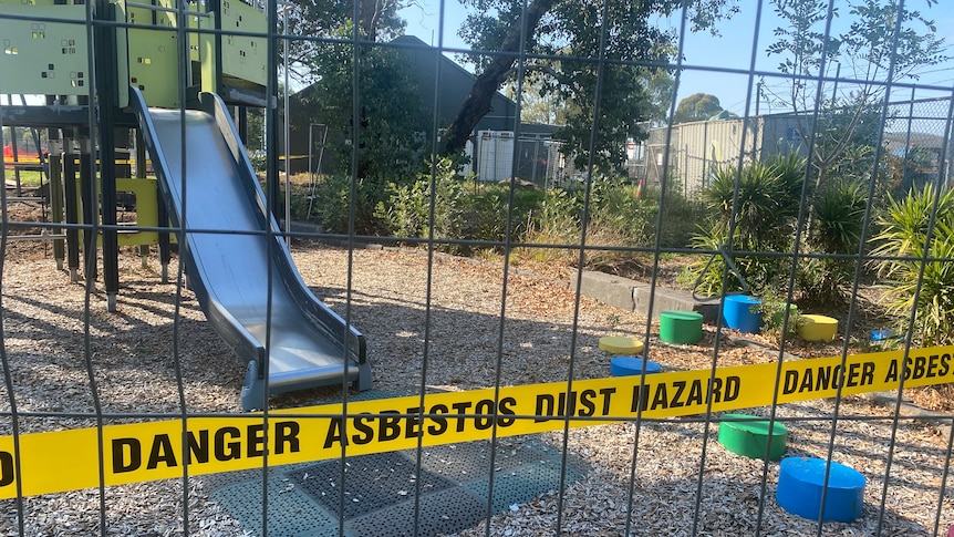 Yellow 'DANGER ASBESTOS DUST HAZARD' tape in front of a playground with a metal slide and gate.