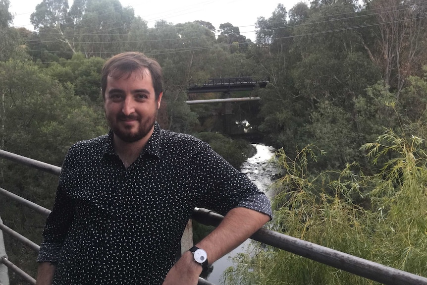An image of Chad Parkhill standing on a bridge with a river and trees behinds him.