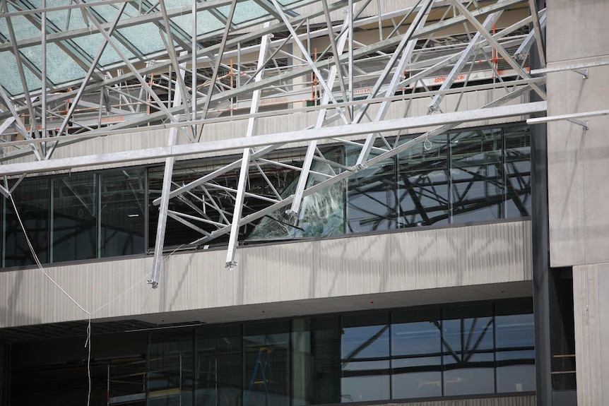 The mangled metal and glass wreckage of a roof hangs over a building after it collapsed.