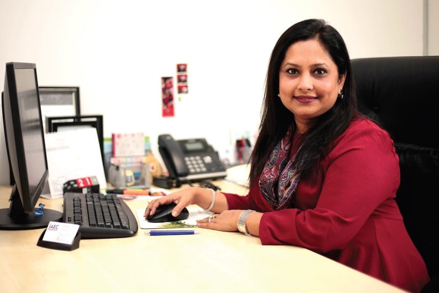 Woman sitting at desk in front of the computer smiles at the camera.