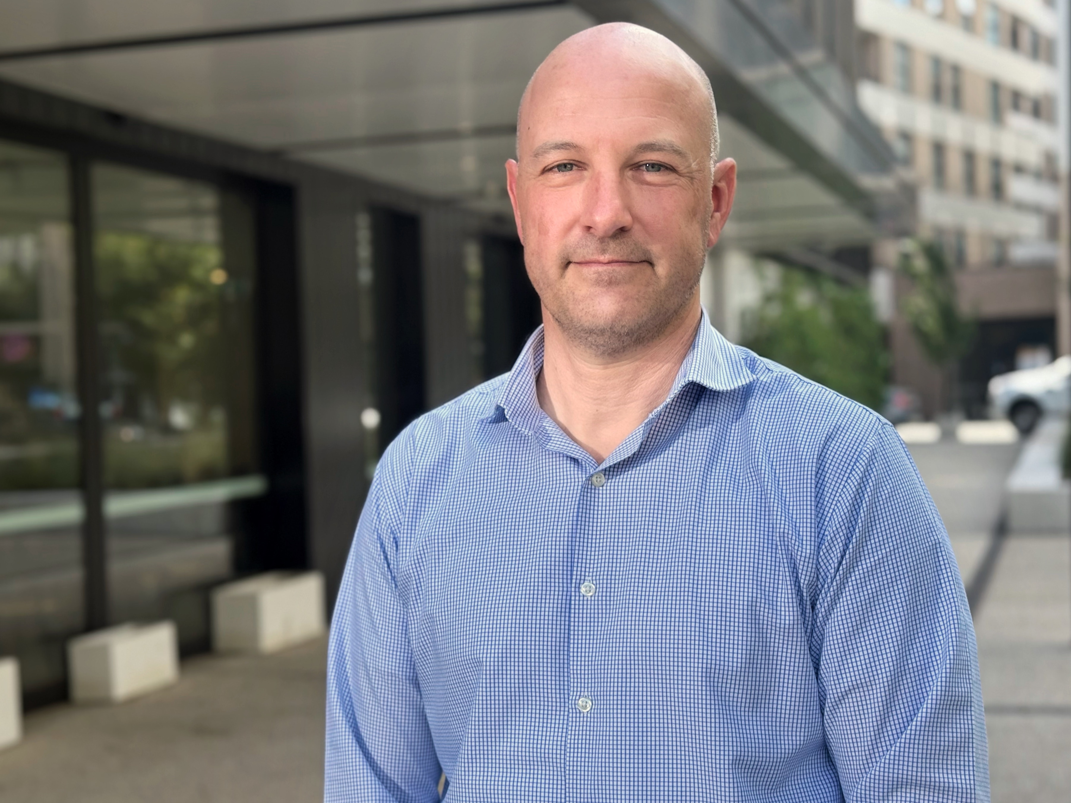 Un hombre con camisa azul sonríe suavemente.