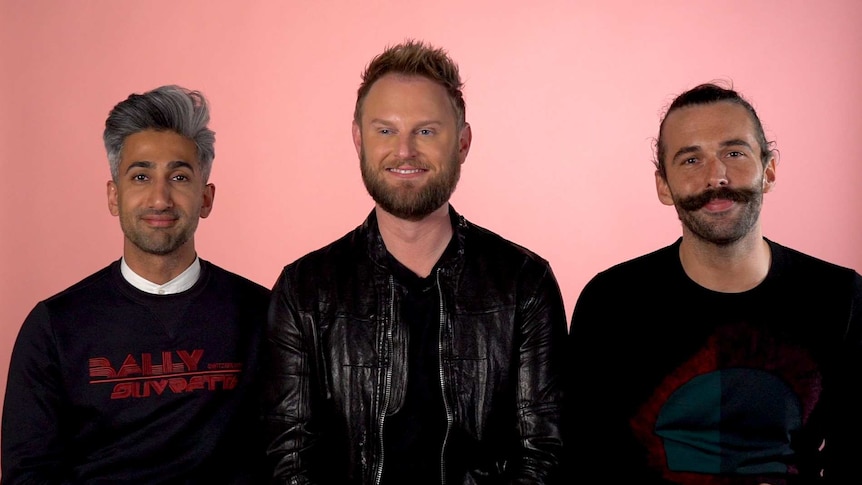 Queer Eye cast members Tan France, Bobby Berk and Jonathan Van Ness seated side by side in front of pink background