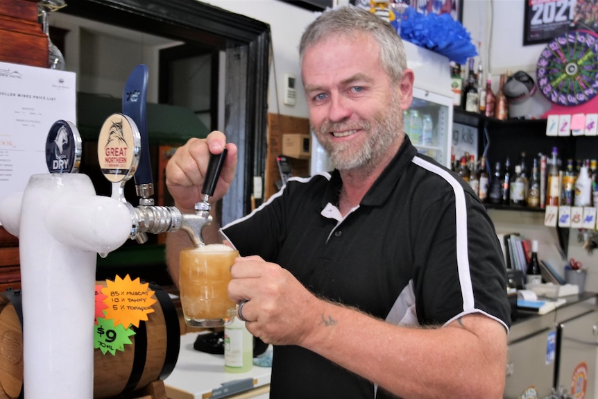 A man standing behind a bar pouring a beer