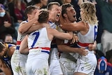 Western Bulldogs players gather for jubilant hugs as disappointed Lions players slump to the ground