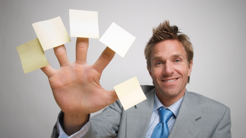 Man in suit holding out hand with small yellow sticky notes stuck to end of each finger
