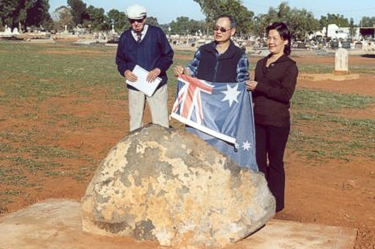 Chinese couple Allan and Patricia Ho holding Australian flag at cemetery plaque site.