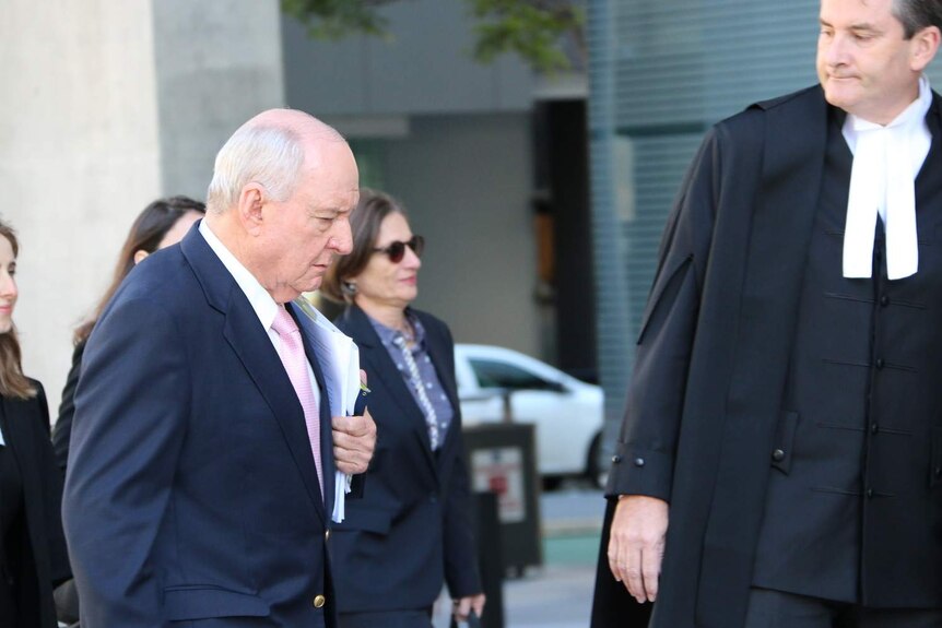 Alan Jones walks on the street carrying papers under his arm